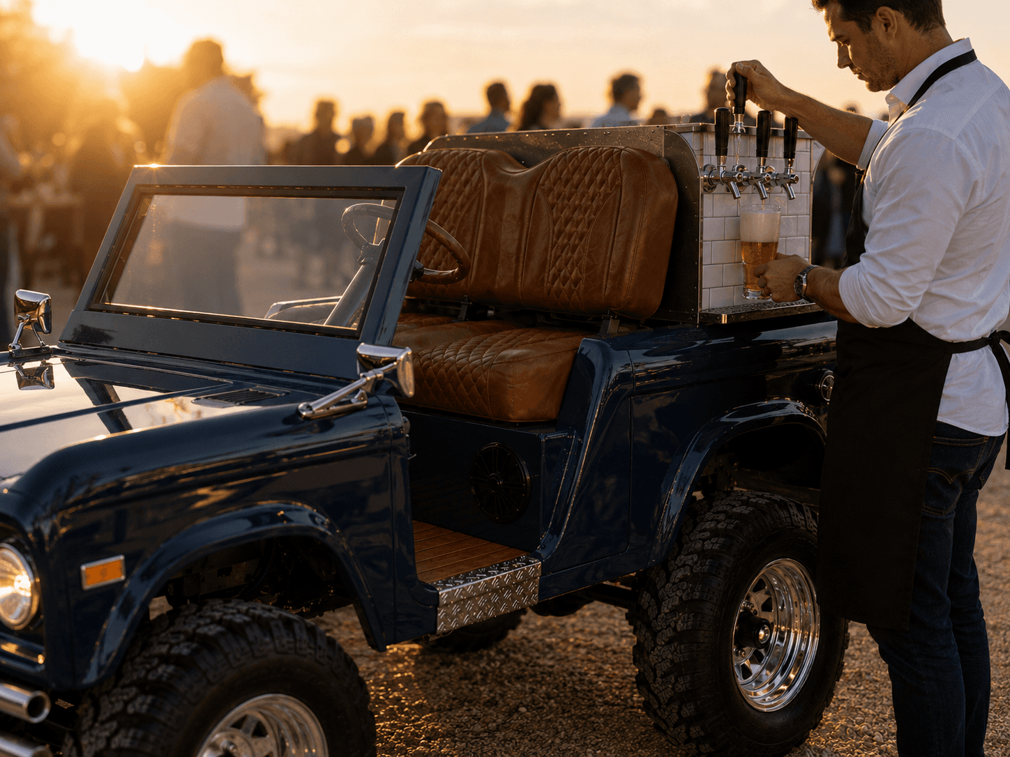 Vintage Bar Co. operator in apron pouring a draft beer from the navy cart's tap tower at a sunset event, crowd softly blurred in the background